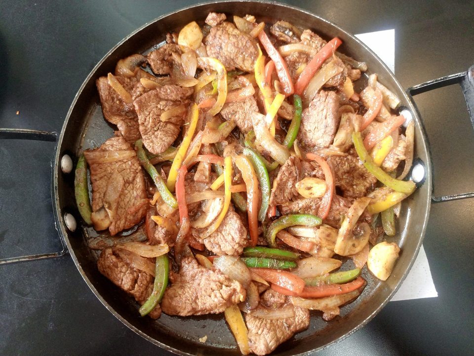 Sliced meat sauteed with colorful bell peppers and onions in a large skillet