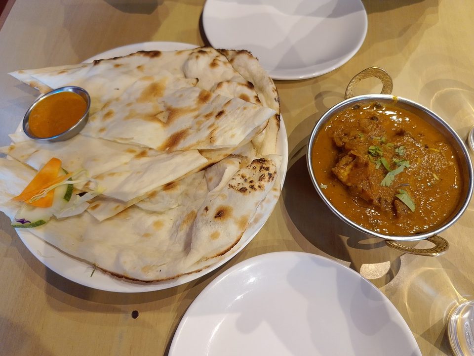 Bowl of spiced curry garnished with cilantro beside a plate of warm naan