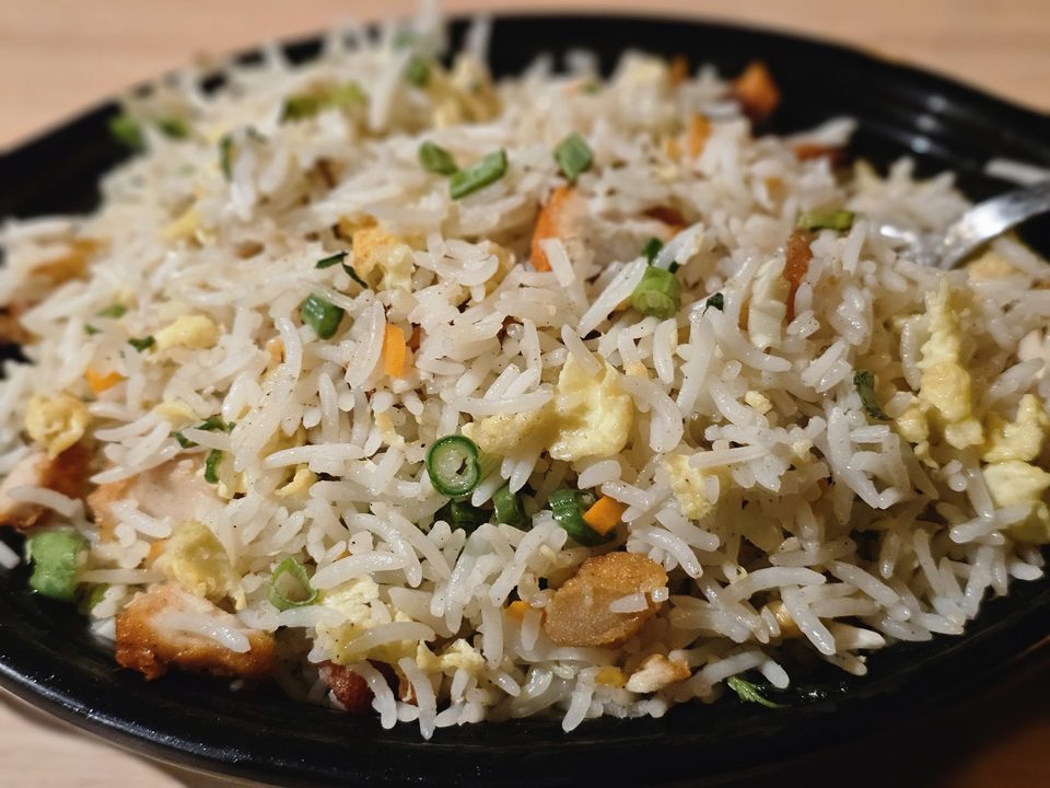 Egg fried rice with scallions, carrots and peas on a black plate