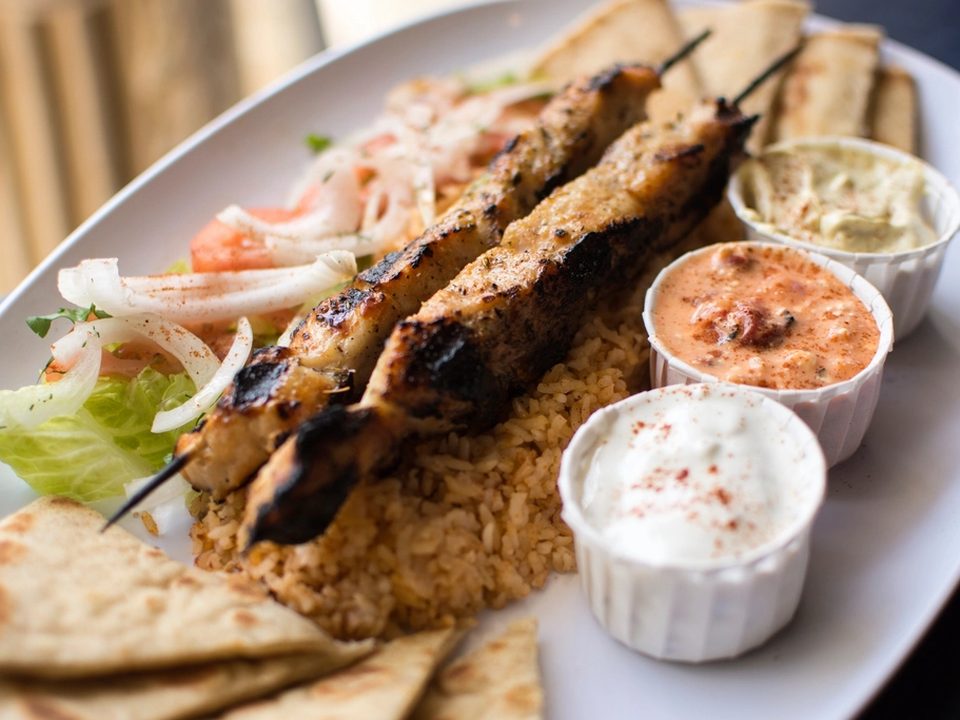 Grilled chicken skewers over rice with pita, tzatziki and dips on an oval platter