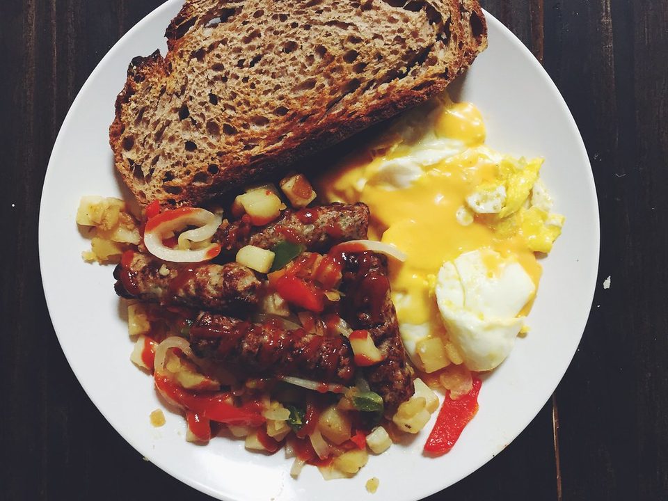 Potato and sausage hash with peppers and eggs on a white plate with toast