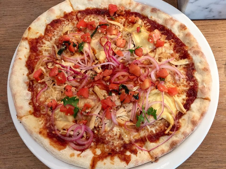Thin-crust pizza topped with tomato, red onion and herbs on a white plate