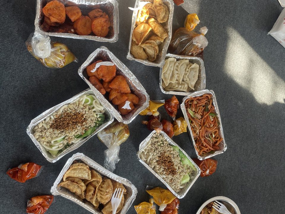 Overhead view of many takeout containers of food spread on a dark surface