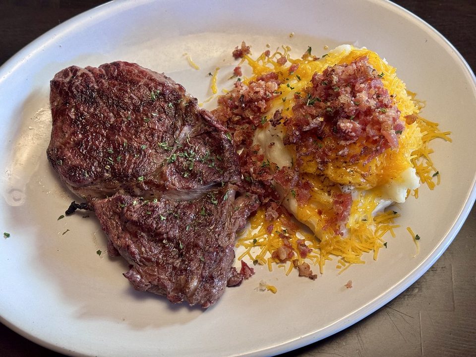 Seared steak on a white platter next to loaded mashed potatoes