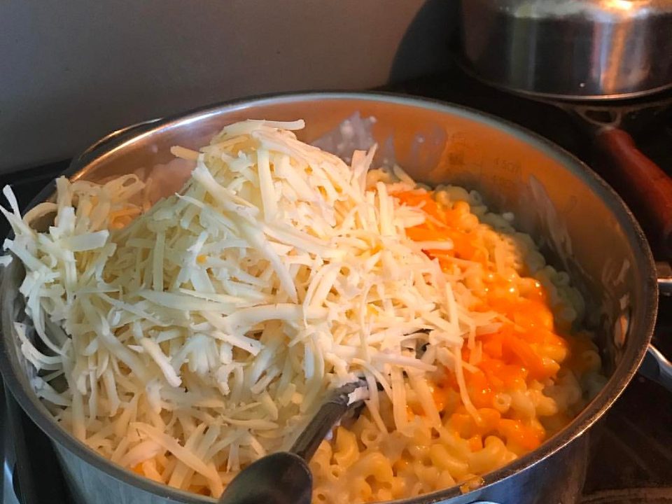 Shredded cheese melting into macaroni in a pot on the stove