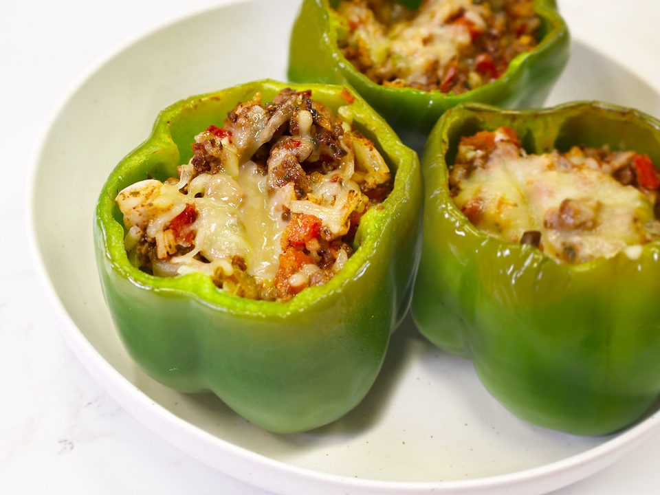 Green bell peppers stuffed with rice, meat and melted cheese in a white bowl
